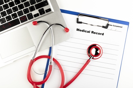 Red stethoscope on  blue clipboard  with medical record close-up with silver colored laptopの写真素材