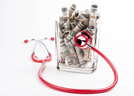 Health in a jar rolled dollars in ajar with a red stesthoscope isolated on white backgroundの写真素材