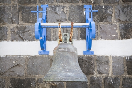 Old church bell on  wall and blue frame held by two rusty chainsの写真素材