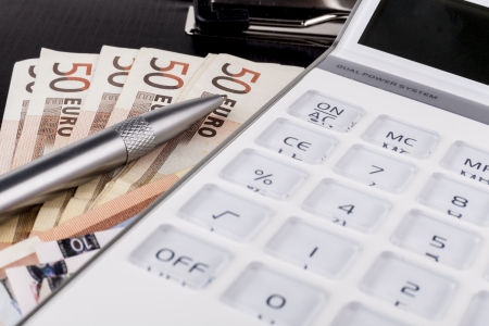 White calculator on top of euro banknotes on black clipboard with silver penの写真素材