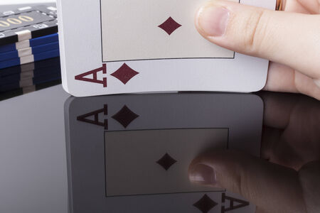 Ace poker card held in hand with reflection on dark table 