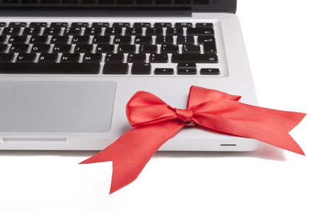 Silver laptop keyboard close-up with red bow isolated on white backgroundの写真素材