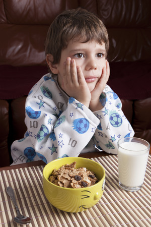 Boy not eating  breakfast cereals and milk on the tableの写真素材