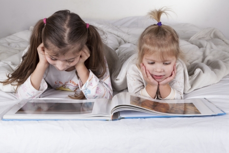 Two sisters reading bad time story in bad with white sheetsの写真素材