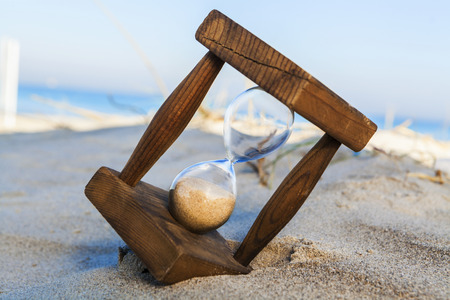 Old wooden houglass in sand on the beach with the sea and blue sky in the backgroundの写真素材