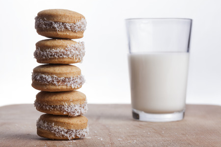 Coconut round cookies tower on wood plate with glass of milk in the backgroundの写真素材