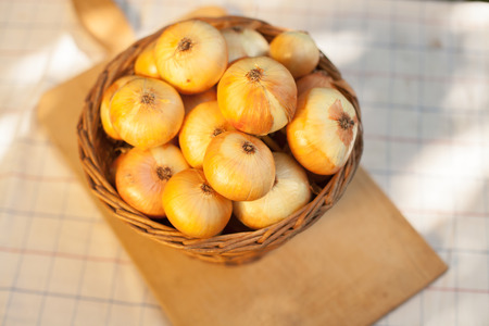 Dry golden onions ina brown basket and cutting woodの写真素材