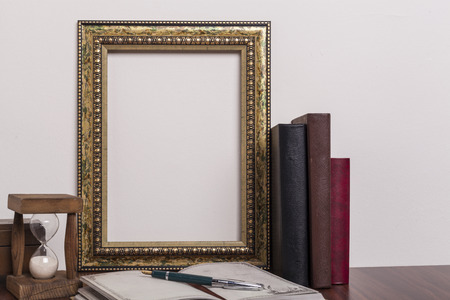 Golden portrait frame with books and horglass on wood tableの写真素材