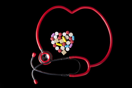 Heart shape Coloerd pills medicine  on black background with red stehoscope