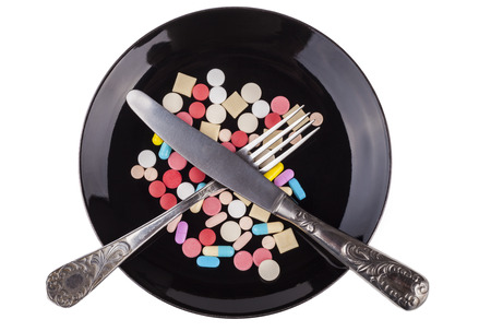 Silver fork and knife on colored pills in  black plate isloated on white backgroundの写真素材