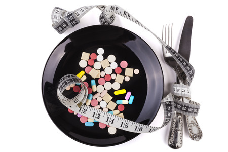 Silver fork and knife on colored pills in  black plate isloated on white backgroundの写真素材