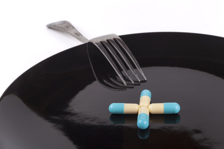 Silver fork with blue pills on black plate isolated on white backgroundの写真素材