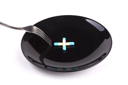 Silver fork with blue pills on black plate isolated on white backgroundの写真素材