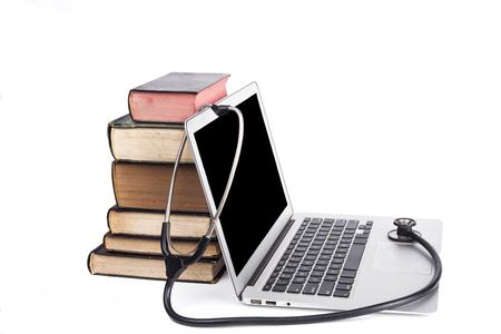 Silver laptop with black stethoscope and old books pile isolated on white backgroundの写真素材
