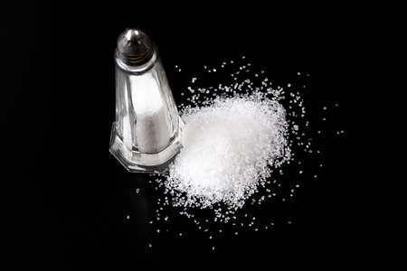 White Salt Shaker with Salt Pile On Black Backgroundの写真素材