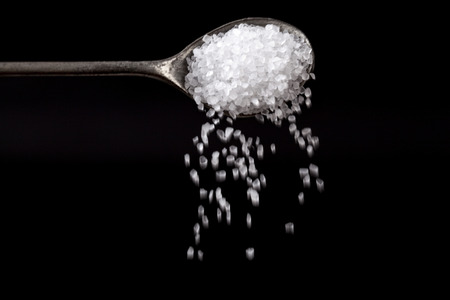 White Sea Salt Crystals Pouring From Silver Spoon on Black Backgroundの写真素材