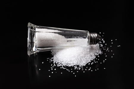 Salt shaker with pured salt crystals on black backgroundの写真素材