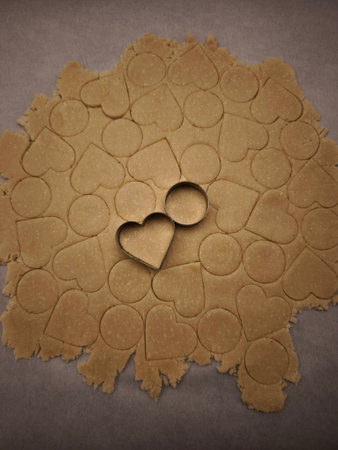 Rolled dough for cookies with heart and circle shapes cut out, metal cookie cutters laying on top, preparing for Valentine's dayの写真素材