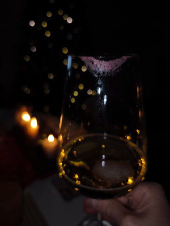 Hand holding a wine glass with a lipstick mark, celebrating Christmas Eve with bokeh lights and candles in the background in Prague holidays new year dinnerの写真素材