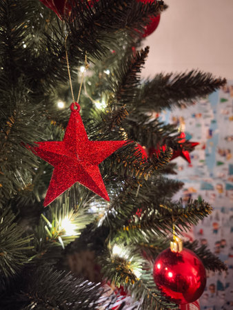 Red glitter star and bauble ornaments hanging on a Christmas tree with lights, adding a festive touch to a cozy prague home during the holiday season New Year preparation decorの写真素材