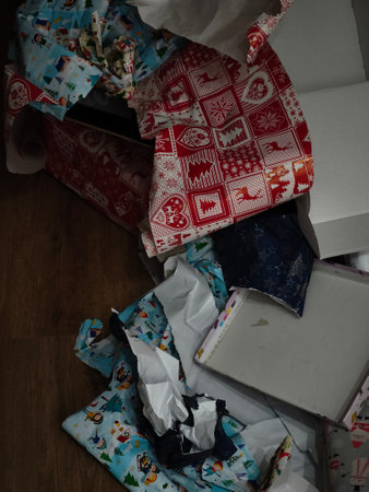 Colorful remnants of christmas wrapping paper and boxes lie scattered on a wooden floor, evidence of a joyful gift opening spreeの写真素材