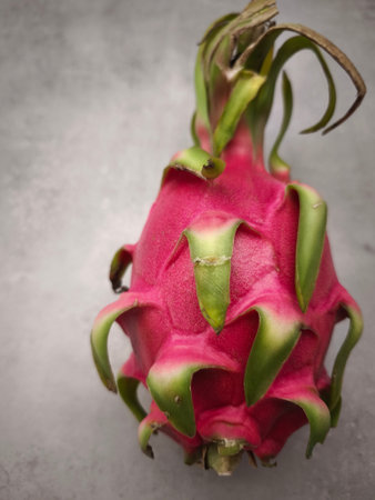 Vibrant dragon fruit with green leaves displayed on a simple gray backdrop, showing freshness and exotic appealの写真素材