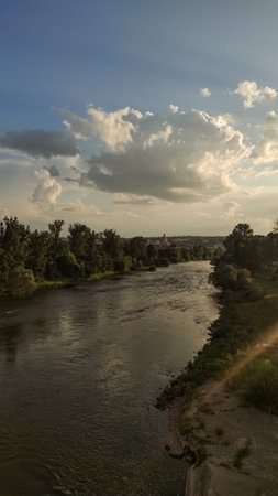 A wide view of a river flowing underneath a blue sky with white clouds.