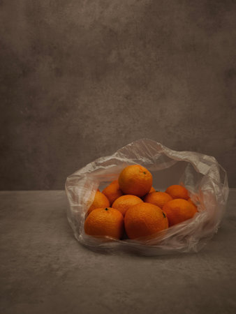 Fresh tangerines resting in plastic bag on gray surface.