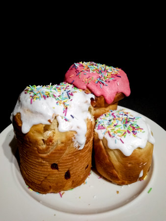 Three easter cakes bread Kulich, decorated with icing and colorful sprinkles, sit on a white plate...