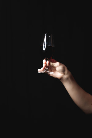 Woman holding glass of red wine against black background, ideal for valentine's day or book cover
