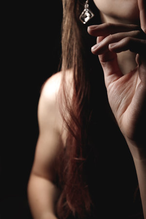 Close up of a woman with long brown hair covering part of her face with her hand, wearing an elegant...
