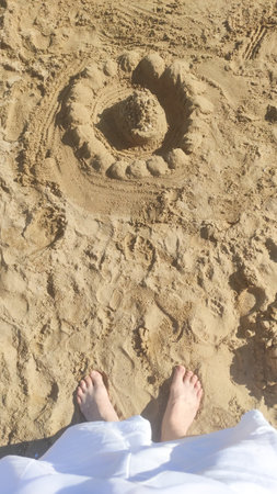 Relaxing tourist enjoying summer beach scene, standing near detailed sandcastle in scenic bibione, italy coastal landscapeの写真素材