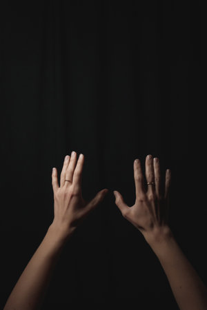 Woman wearing wedding rings, hands lifted skyward, silhouetted against shadowy backdrop, symbolizing romantic devotion and personal grace dark backgroundの写真素材