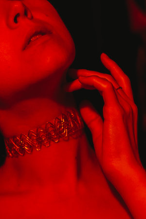 Close up of a woman's neck adorned with a detailed wire necklace, her hand gently touching her chin,...