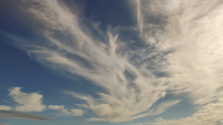 Wispy cirrus clouds create a mesmerizing pattern against the vibrant blue sky, capturing the essence...