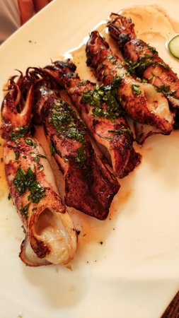 Grilled squids seasoned with fresh herbs, served on a white plate, representing a typical croatian...