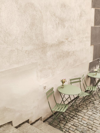 Green bistro tables and chairs sit empty on a cobblestone street alongside a weathered wall in cesky krumlov, czechia, waiting for customers to arriveの写真素材