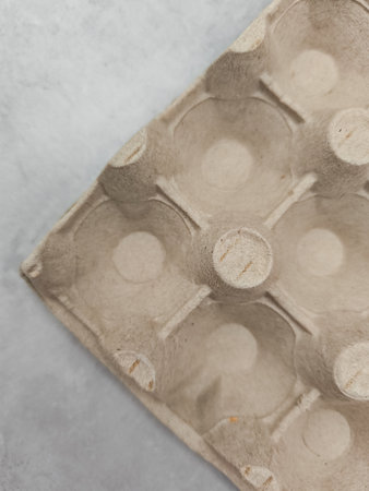 Close up of an empty egg carton resting on a gray surface, suggesting preparation for easter or...