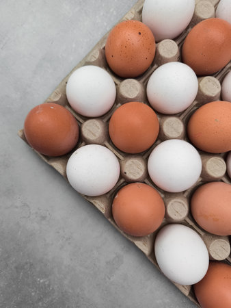 Carton of fresh brown and white eggs, perfect for breakfast, baking, or cooking, lying on a gray tableの写真素材