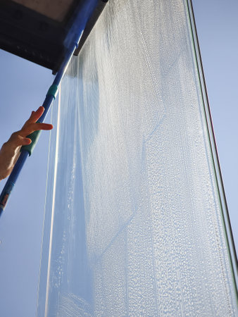 Professional cleaning service washing windows of modern office building facade with telescopic water...