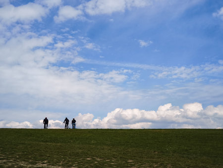 Cyclists pedaling through verdant landscape, silhouetted against dramatic cloudy skyline, experiencing serene outdoor adventureの写真素材