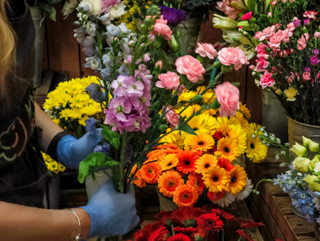 Florist wearing blue gloves arranging a bouquet of colorful flowers in a flower shop, surrounded by...
