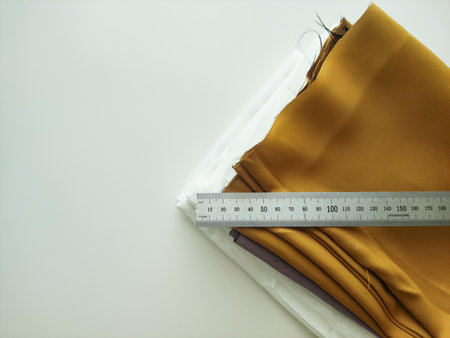 Warm mustard and crisp white fabric swatches neatly stacked on a smooth surface, measuring ruler placed across the top, showcasing the rich textures and colors ideal for creative design projectsの写真素材