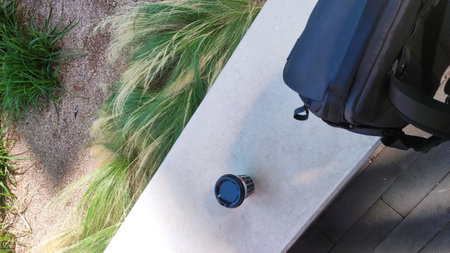 Disposable coffee cup and backpack resting on a concrete ledge next to ornamental grass, suggesting...