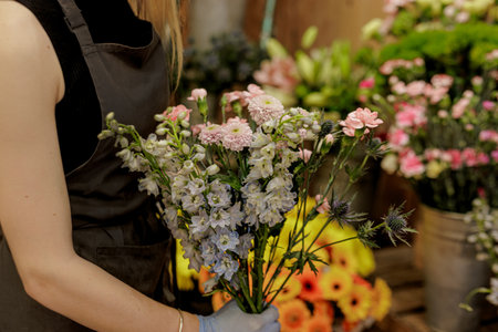 Florist wearing gloves carefully arranging a bouquet of colorful larkspur, carnations, and eryngium...