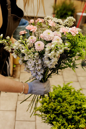 Florist wearing gloves skillfully arranging a vibrant bouquet of pink and blue flowers in a charming flower shop, showcasing floral artistry, Mothers dayの写真素材