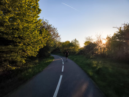 Athlete running along a paved road at sunset, capturing the serene beauty while embracing an active lifestyleの写真素材