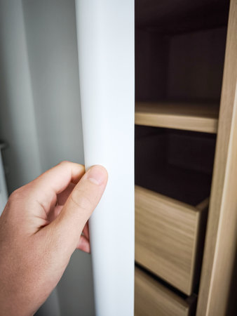 Modern bedroom wardrobe with a sleek design, featuring open shelves and drawers, hand reaching for the door, ideal for stylish storage solutionsの写真素材