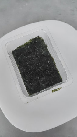 Close up of a single dried seaweed sheet, neatly packaged in a plastic tray, resting on a pristine...