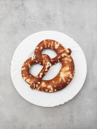 Freshly baked pretzel resting on white plate, top view of traditional snackの写真素材